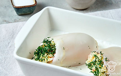 Нафаршируйте и приготовьте кальмары. Очищенный кальмар заполните начинкой, выложите его в форму для запекания. Сверху залейте сметаной с водой и поставьте запекаться в духовку на 30 минут.