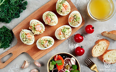 Для праздничной подачи выложите на плоское блюдо салатные листья. Сверху распределите фаршированные яйца. Украсьте оставшимися креветками, разрезанными пополам.