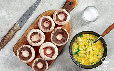 Подготовьте ингредиенты. Для этого удалите у шампиньонов ножки, стараясь при этом не повредить шляпку. Далее на каждой шляпке сделайте надрезы в виде креста и слегка посолите внутри. Зеленый лук и кинзу измельчите, а чеснок очистите и пропустите через пресс. Куриные яйца разбейте в отдельную миску. Добавьте к ним чеснок, зелень, тертый сыр. Приправьте смесь солью и перемешайте.