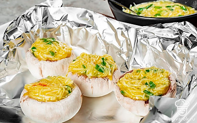 Приготовьте блюдо. Готовую яичную начинку выложите внутрь грибных шляпок, прижимая ее ложкой. Духовку включите разогреваться до 180 градусов. На противень поместите лист фольги, сверху выложите фаршированные шампиньоны. Аккуратно заверните закуску в фольгу, отправьте ее в духовку на 25-30 минут.