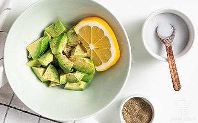 Начните приготовление. Авокадо разрежьте на две части, удалите косточку, а мякоть аккуратно извлеките из кожуры, нарежьте кубиками и положите в миску. Туда же добавьте лимонный сок, соль и перец по вкусу. Готовую смесь перемешайте.