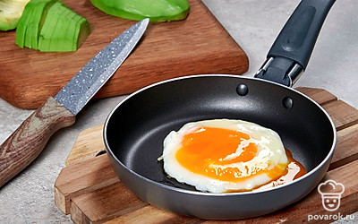 Начните готовить тост. Тонкими слайсами нарежьте авокадо или измельчите его в пюре. На хорошо разогретой сковороде, сбрызнутой маслом, поджарьте яйцо в течение 3-5 минут.