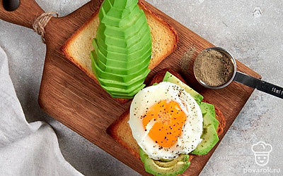Сформируйте тост. На кусочек хлеба уложите авокадо, поверх — поджаренное яйцо. Присыпьте небольшим количеством соли и перца.