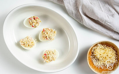 Приготовьте фаршированные яйца в духовке. Яичные белки выложите в форму для запекания, застеленную пергаментом. Заполните каждую начинкой с горкой. Посыпьте тертым пармезаном. Запекайте при 160 градусах до румяного цвета 15-20 минут.