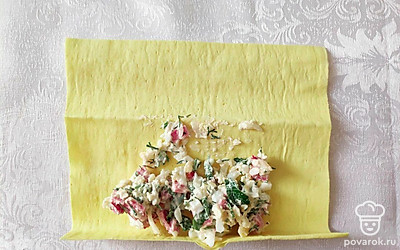 При помощи кухонных ножниц разрежьте лаваш на крупные квадраты. На один край квадрата выкладывайте по две столовые ложки начинки и закручивайте рулетики.