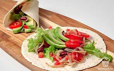 Приготовьте блюдо. Возьмите одну тортилью, положите на нее лист салата. Добавьте 2 ст. л. готовой начинки с фасолью и несколько кружочков помидоров черри. Сверху выложите ломтики авокадо, полейте их 1 ч. л. сока лайма. После этого заверните боковые края тортильи внутрь, к начинке. Подогните нижний край лепешки и заверните блюдо в рулет в направлении от себя. Повторите действия со всеми тортильями.