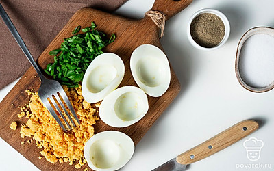 Подготовьте основу для закуски. Яйца сварите вкрутую, остудите с помощью холодной воды, удалите скорлупу. Разрежьте вдоль посередине на две равные части. Желток измельчите. Половинки белка оставьте в неизменном виде.