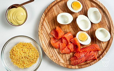 Сделайте начинку. Яйца разрежьте пополам, извлеките желтки и разомните их вилкой. К желткам добавьте майонез и тщательно перемешайте до однородного состояния. Семгу нарежьте тонкими полосками и сверните их в рулетики.