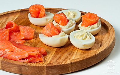 Зафаршируйте яйца. Приготовленной смесью нафаршируйте белки. На каждую половинку яйца сверху выложите рулетик из семги.