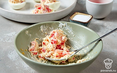 Приготовьте фаршированные яйца. В миску выложите желток и разомните вилкой. Добавьте туда сыр, помидор, посолите и положите майонез со сметаной. Затем положите чеснок и перемешайте. Аккуратно выложите готовую начинку в белки.