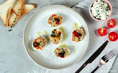 Фаршированные яйца положите на квадратную тарелку, каждую "лодочку" украсьте половинкой томатов черри и маслиной.