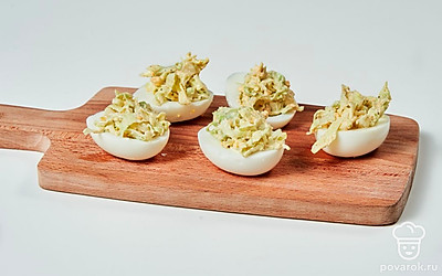 Нафаршируйте яйца. Желток мелко натрите и соедините в отдельной миске с капустой и майонезом. Посолите, поперчите, сбрызните лимонным соком. Перемешайте. Начинку выложите в пустые половинки яичных белков. Посыпьте сверху каждую половинку тертым сыром.