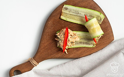 Сформируйте закуску. На тарелку уложите две полоски кабачка, сверху распределите начинку и добавьте кусочек болгарского перца. Сверните начинку в рулет.