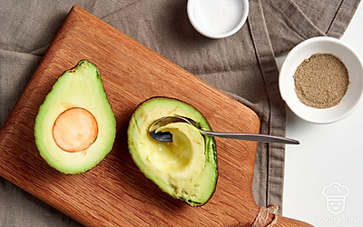 Начните приготовление. Используя ложку, увеличьте углубление от косточки, чтобы в авокадо могло поместиться яйцо. После этого сделайте из фрукта прочную «тарелку», срезав для этого немного кожуры. Полученную основу переложите в форму.