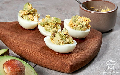 Приготовьте фаршированные яйца. Авокадо мелко нарежьте. Выжмите сок лимона на авокадо. Желтки выложите в отдельную миску с авокадо и разомните вилкой. Добавьте к ним сметану, посолите и поперчите. Тщательно перемешайте и выложите по 1 ч. л. начинки в белки.