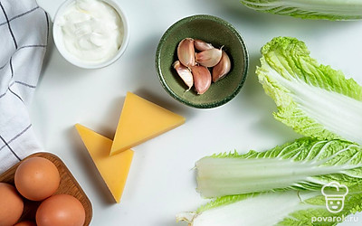 Отварите яйца вкрутую в течение 8 минут после закипания на небольшом огне. Остудите, почистите и разрежьте вдоль. Достаньте желтки. Сыр натрите на мелкой терке. Почистите и помойте чеснок, пропустите его через пресс. Промойте, просушите и нашинкуйте базилик. Помойте и обсушите салатные листья.