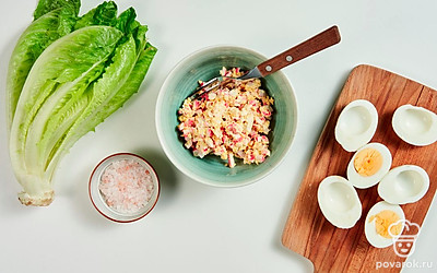 Приготовьте начинку. Яйца разрежьте вдоль пополам, извлеките желтки и натрите их на терке. Крабовые палочки мелко покрошите, смешайте с желтком, посолите и добавьте майонез.