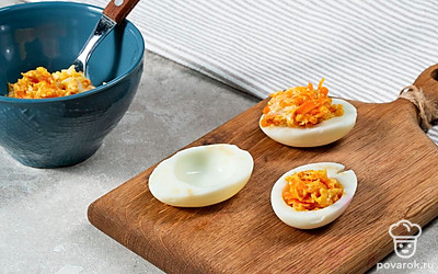 Сделайте начинку и нафаршируйте яйца. В небольшую емкость выложите обжаренную морковь и измельченные желтки. Посолите и поперчите, добавьте майонез и тщательно размешайте. Масса должна получиться мягкой, поэтому при желании пюрируйте начинку блендером. Половинки куриных белков наполните начинкой, примерно по 2 ч. л.