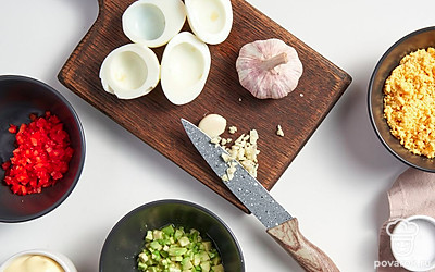 Подготовьте ингредиенты для начинки яиц. Яйца разрежьте пополам. Желтки уберите и измельчите. Красный сладкий перец нарежьте мелкими кубиками и сбрызните растительным маслом. Авокадо очистите от косточки и извлеките мякоть. Сбрызните соком лимона. Чеснок мелко нашинкуйте.