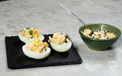 Наполните яйца начинкой. Намажьте половинки яиц желтковой массой. Украсьте листочками петрушки и половинками маслин.