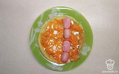 Каждый блин смажьте сыром фета, выложите горсть моркови по-корейски и сосиски. Блин с начинкой заверните в трубочку.