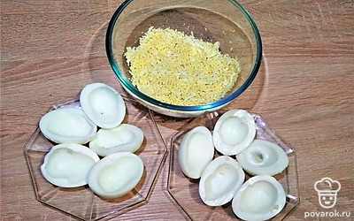 Куриные яйца отварите вкрутую (около 10 минут с момента закипания), очистите от скорлупы и разрежьте вдоль на две половинки каждое. Выньте желтки и перетрите их на мелкой терке или растолките вилкой.