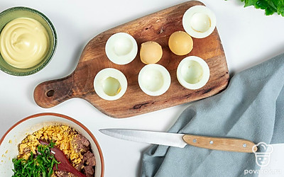 Сделайте начинку. Отваренные яйца очистите, разрежьте на половинки и достаньте желтки, поместите их в отдельную миску. Листики петрушки отделите от стеблей и мелко нарежьте. К желткам добавьте печень трески, майонез и зелень, разомните все вилкой до однородной массы и хорошо перемешайте.