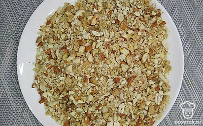 На разделочной доске измельчите орехи. Поставьте сковороду на огонь, отправьте в нее измельченные орешки и прожарьте до золотистого цвета.