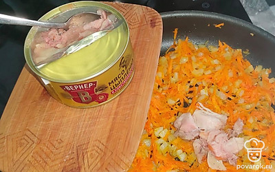 Когда лук станет прозрачным в зажарку добавьте тушенку. Перемешайте, жарьте на среднем огне 10-15 минут. 