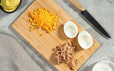 Подготовьте начинку. Яйца поделите пополам острым ножом и достаньте желток, который измельчите на терке или разомните вилкой. Скумбрию порежьте мелкими кубиками.