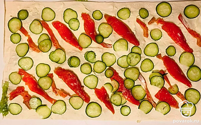 После накройте промазанный первый слой лаваша вторым листом лаваша, также смажьте его оставшейся творожной массой и присыпьте по желанию укропом. Затем равномерно разложите нарезанные ломтики красной рыбы, а между кусочками семги разложите тонко нарезанные кружочки огурца.