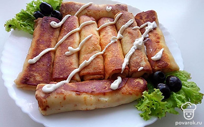 Выложите блины на тарелку и украсьте их листьями салата и оливками, а на сами блины налейте немного сметане.