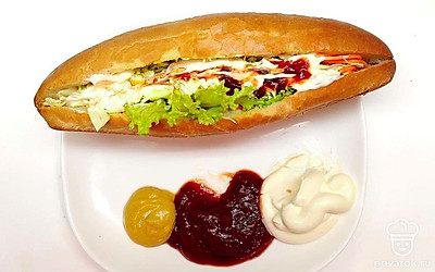 В готовую булку ставьте лист салата, затем корейскую морковь, и капусту. Сверху положите сосиску и заправьте соусом.