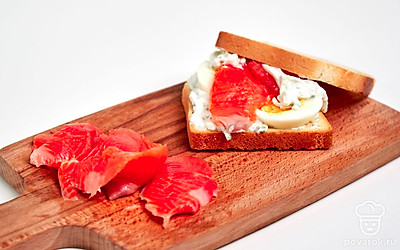 Соберите тосты. Обжаренный ломтик хлеба намажьте соусом, далее положите два колечка яйца, затем ломтик рыбы, сверху снова добавьте немного соуса. Накройте вторым ломтиком хлеба. Таким же образом соберите второй тост.