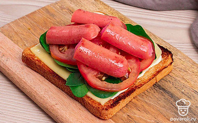 Тост смажьте соусом. Соберите сэндвич, выложите сыр, на него салат, овощи и сосиски. Приятного аппетита!