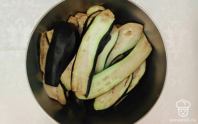 Отрежьте хвостики у баклажанов, затем разрежьте их вдоль на пластины, толщиной не более 0.7 см. Разогрейте сковороду, обжаривайте пластины около 3-4 минут с каждой стороны. В это время почистите чеснок.