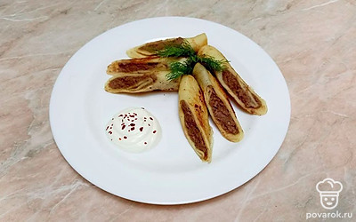 Уложите на широкое блюдо блинчики, разрезав каждый на две половины и украсив зеленью. Рядом расположите сметану.