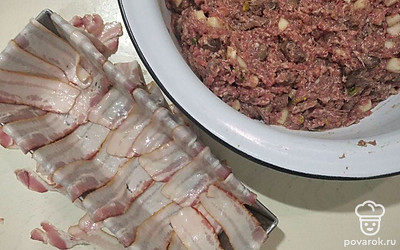 Подготовьте форму для выпечки. В форму для выпечки выложите на дно (внахлест) нарезанный бекон, так чтобы оставались кусочки, которым можно будет накрыть верхнюю часть. Поверх бекона выложите фарш, разровняйте силиконовой лопаткой, а оставшимися кусочками бекона накройте выложенный фарш.