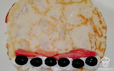 Отступите 2-3 сантиметра от края блина и выложите полоску творога. Сразу за ним расположите рыбные ломтики, а маслины положите на творог. Начинку посыпьте итальянскими травами и туго сверните блин рулетиком. Те же операции проделайте со всеми получившимися блинами.