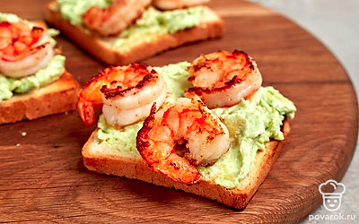 Соберите тосты. Ломтики хлеба разрежьте пополам. Подсушите их на сухой сковороде или поджарьте в тостере. На хлеб намажьте массу из авокадо. Сверху положите креветки.