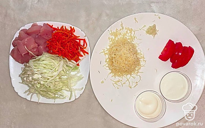 Нашинкуйте капусту. Курицу нарежьте мелким кубиком. Чеснок пропустите через пресс, сыр натрите на мелкой терке. Порежьте помидоры полукольцами.