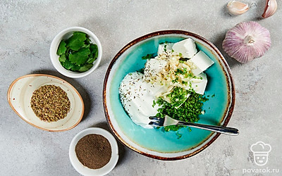 Приготовьте начинку. В миску выложите фету, сметану, добавьте измельченный чеснок и кинзу. Всыпьте сухой орегано и черный перец. Тщательно разомните начинку вилкой. Заполните ею нижнюю часть помидоров.