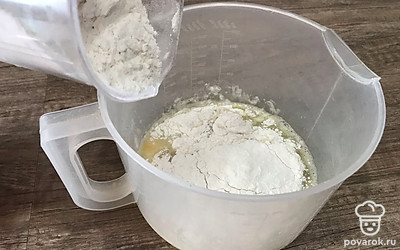 Добавьте просеянную муку и хорошо перемешайте, постепенно добавляя остаток всей жидкости.