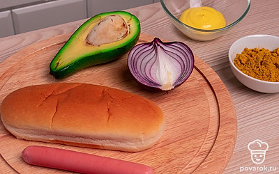 Подготовьте все ингредиенты и выложите их на стол. Снимите пленку с сосисок. Помойте авокадо и под проточной водой, затем очистите его и репчатый лук.