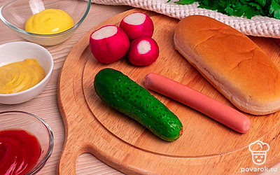 Подготовьте все ингредиенты и выложите их на стол. Снимите пленку с сосисок. Помойте редис, огурец и петрушку под проточной водой.