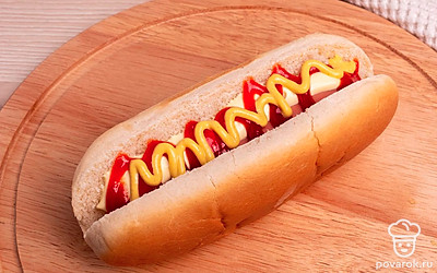 Возьмите булочку для хот-дога, разрежьте ее вдоль по центру, но не до конца. Смажьте булочку кетчупом, майонезом и горчицей внутри с обеих сторон.