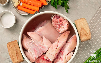 Отварите холодец. В кастрюлю положите мясные части, залейте водой, доведите до кипения и снизьте температуру. Варите, снимая пену, в течение 6 часов. За 1,5 часа до готовности добавьте к мясу морковь, лук, чеснок, соль и перец. Снимите с огня и достаньте мясо и овощи из бульона. Морковь порежьте круглыми ломтиками, мясо разберите на волокна.