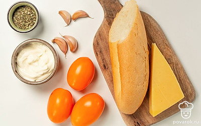 Удобно расположите нужные продукты. Багет нарежьте на тонкие ломтики. Помидоры вымойте, нарежьте тонкими кольцами. Сыр натрите на мелкой терке. Зубчики чеснока почистите, вымойте и пропустите через пресс. Зелень для подачи вымойте и обсушите.