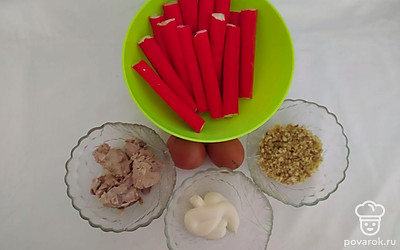 Крабовые палочки разморозьте и разверните. Чтобы крабовые палочки хорошо разворачивались, опустите их на 30 секунд в кипяток. Яйца сварите вкрутую. Орехи измельчите в комбайне или вручную. Банку с печенью трески откройте, процедите через дуршлаг, чтобы избавиться от маринада и разомните ее вилкой.