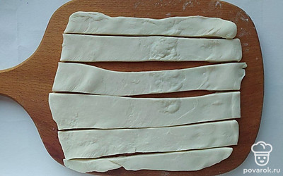 Раскатайте слоеное тесто на доске присыпанной мукой. Нарежьте тесто на полоски шириной в 2 см. Застелите противень пергаментной бумагой.